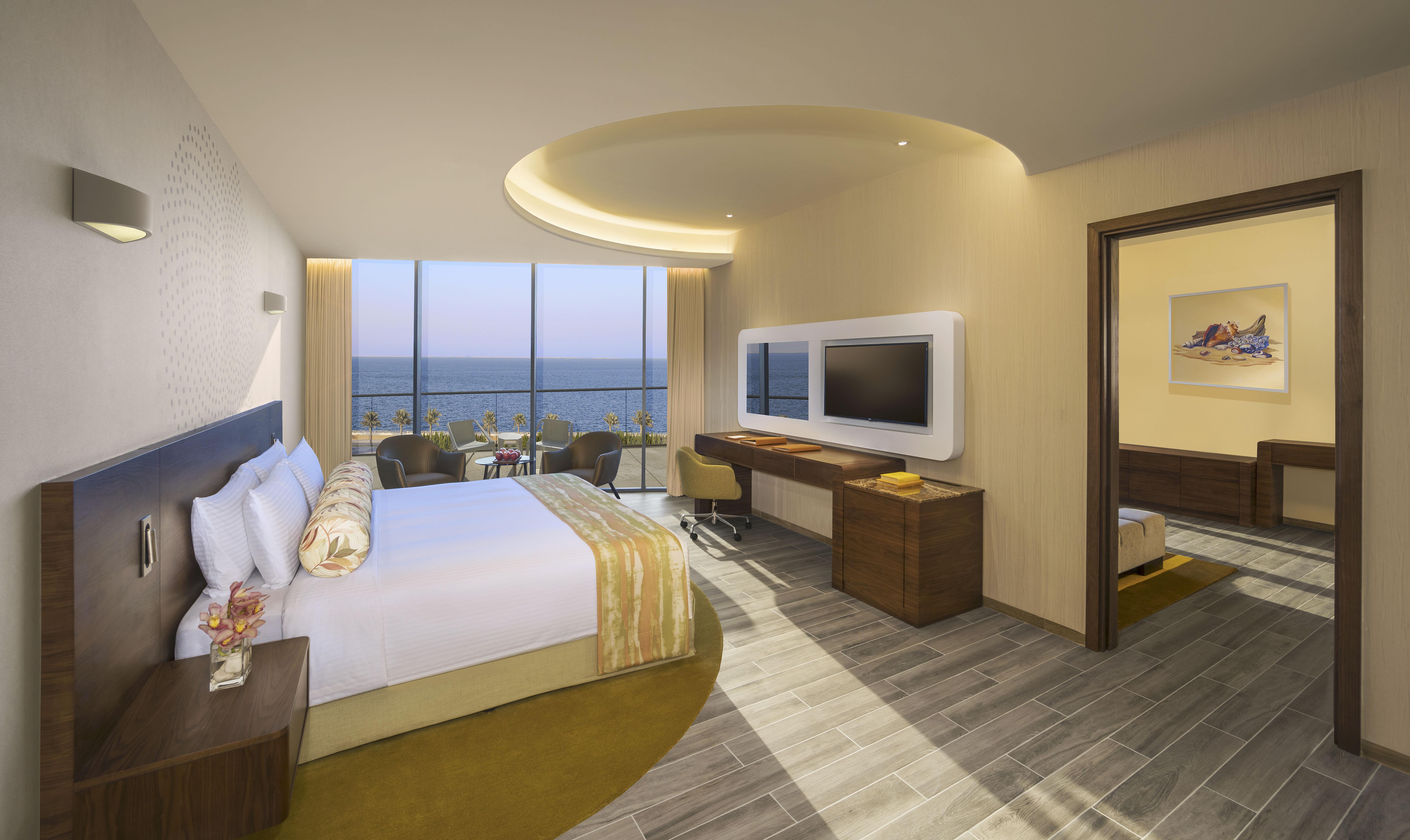 The Retreat Palm Dubai Mgallery By Sofitel Kültér fotó The photo depicts a modern hotel room featuring a large bed with white and yellow bedding. The room is well-lit with natural light coming through large glass windows that offer a view of the ocean. There is a comfortable seating area and a flat-scree