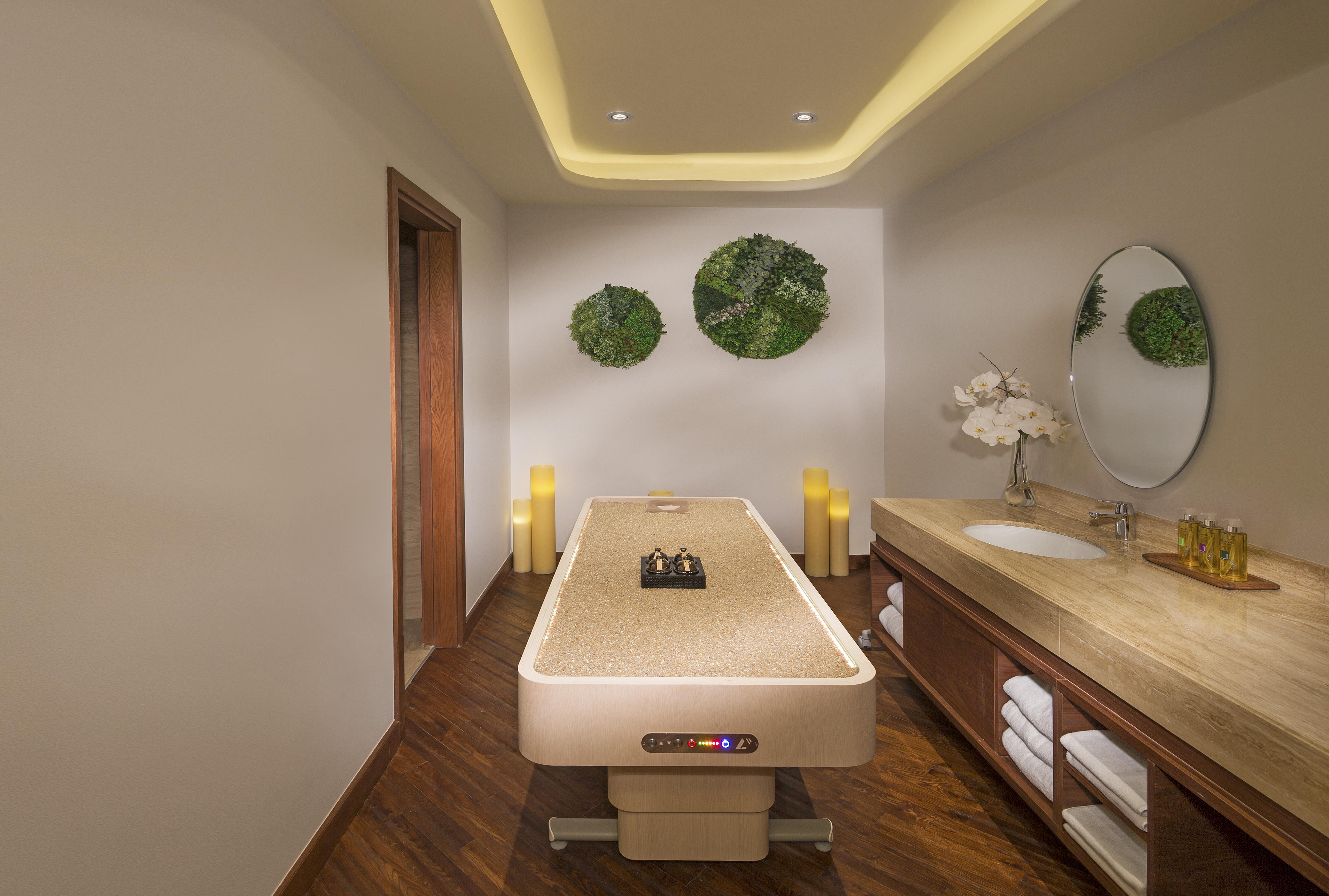 The Retreat Palm Dubai Mgallery By Sofitel Kültér fotó The photo shows a serene spa room designed for relaxation and wellness. In the center, there is a massage table with a smooth surface, likely ready for treatments. The walls are decorated with round green wall art that appears to consist of natural m